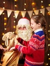 Child girl accepting gifts from Santa near decorated xmas tree with lights, they talking and smiling - Merry Christmas and Happy Royalty Free Stock Photo