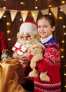 Child girl accepting gifts from Santa near decorated xmas tree with lights, they talking and smiling - Merry Christmas and Happy Royalty Free Stock Photo