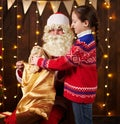 Child girl accepting gifts from Santa near decorated xmas tree with lights, they talking and smiling - Merry Christmas and Happy Royalty Free Stock Photo