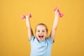 Child girl is doing exercises with dumbbells on yellow studio background. Sport portrait kids. Royalty Free Stock Photo