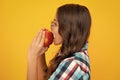 Child girl eating an apple over  yellow studio background. Close up face of tennager with fruit. Portrait of Royalty Free Stock Photo