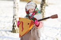 Child girl in a fur coat and a scarf in Russian with a balalaika