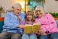 Child girl granddaughter with grandparents reading interesting book together sitting on home couch Royalty Free Stock Photo