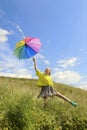 Child a girl with a great mood jumps in the summer in a field with a rainbow umbrella