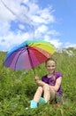 Child a girl with a great mood is sitting in a summer field with a rainbow umbrella