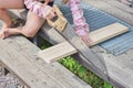 The child girl with a hacksaw saws a board outside photo without processing