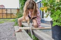 The child girl with a hacksaw saws a board outside photo without processing