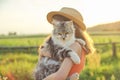 Child girl in hat with gray fluffy cat in her arms. Beautiful sunset country landscape background Royalty Free Stock Photo
