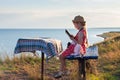 Child girl in a straw hat and dress sitting on bench and reading book. Cute kid with soft rabbit toy looking at notebook Royalty Free Stock Photo