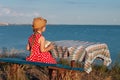 Child girl in a straw hat and dress sitting on bench and reading book. Cute kid with soft rabbit toy looking at notebook Royalty Free Stock Photo