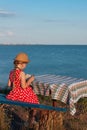 Child girl in a straw hat and dress sitting on bench and reading book. Cute kid with soft rabbit toy looking at notebook Royalty Free Stock Photo