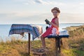 Child girl in a straw hat and dress sitting on bench and reading book. Cute kid with soft rabbit toy looking at notebook Royalty Free Stock Photo