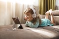 Child girl in headphones is using a digital tablet sits on the sofa at home.