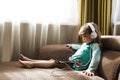 Child girl in headphones is using a digital tablet sits on the sofa at home.