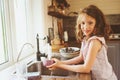 Child girl helps mother at home and wash dishes in kitchen. Casual lifestyle in real interior