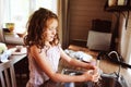 Child girl helps mother at home and wash dishes in kitchen. Casual lifestyle in real interior