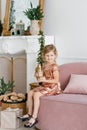 A child girl holds a wooden toy horse in her hands and sits on the sofa near a Christmas tree Royalty Free Stock Photo