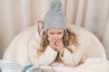 Child girl at home in chair with warm knitted hat woolen blanket sneezes in handkerchief. Season autumn winter colds