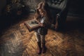 Child girl in image of Sherlock Holmes stands in room and looks photoalbum with magnifier on background of old interior. Closeup. Royalty Free Stock Photo