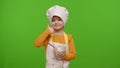 Child girl kid dressed as professional cook chef stir flour in plate, smiling, showing thumb up Royalty Free Stock Photo