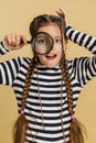 Child girl kid holds magnifying glass near face looking at camera with big zoomed eye, analyzing Royalty Free Stock Photo