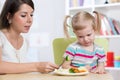 Child girl looks with disgust at healthy vegetables. Mother convinces her daughter to eat food. Royalty Free Stock Photo