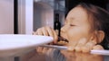 Child girl is opening a fridge, taking an eclair and eating it furtively.