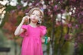 Child girl in pink dress blowing soap bubbles in nature against background of blooming tree Royalty Free Stock Photo