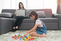 Child girl playing with colorful toy blocks and Young mother using notebook on sofa in living room at home Royalty Free Stock Photo