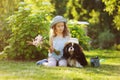 child girl playing with her spaniel dog in summer garden, both wearing funny gardener hats