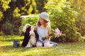 Child girl playing with her spaniel dog in summer garden, both wearing funny gardener hats, holding bouquet