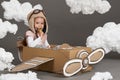 The child girl plays in an airplane made of cardboard box and dreams of becoming a pilot, clouds of cotton wool on a gray backgrou