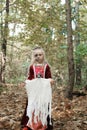 A child girl poses in a forest in a medieval dress in the image of a dead princess with makeup on her face. Girl holding