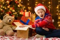 Child girl posing in new year or christmas decoration, wearing a red sweater and a Santa hat, she opening a gift box and having Royalty Free Stock Photo