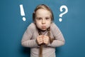 Child girl with question and exclamation marks on the background of blue wall. Idea, solution concept