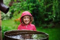 Child girl in red raincoat playing with water barrel in rainy summer garden. Water economy and nature care Royalty Free Stock Photo