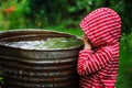 Child girl in red raincoat playing with water barrel in rainy summer garden. Water economy and nature care Royalty Free Stock Photo