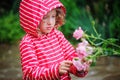 Child girl in red striped raincoat playing with wet roses in rainy summer garden. Nature care concept. Royalty Free Stock Photo