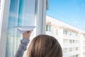 Child girl, releases a paper plane from a plastic window, against the sky, close-up