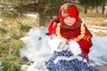 Child girl in Russian pavloposadskie folk scarf on head with floral print and with bunch of bagels on background of snow. Royalty Free Stock Photo