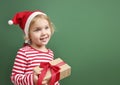 Child girl in santa red hat with box on green empty space background.Kid with christmas gift Royalty Free Stock Photo