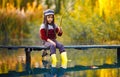 Child girl sits on wooden fishing bridge and catches fish in autumn. Royalty Free Stock Photo