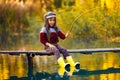 Child girl sits on wooden fishing bridge and catches fish in autumn.