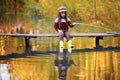 Child girl sits on wooden fishing bridge and catches fish in autumn. Royalty Free Stock Photo