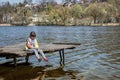 Child girl sits on wooden fishing bridge and catches fish with self-made fishing rod in spring