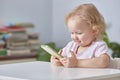 child girl is sitting at a table with a phone in her hands and smiling while looking at a smartphone.