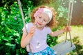 Child girl smells flower on swing in summer garden