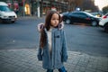 Child girl is standing at the sidewalk on background of city street in evening. Royalty Free Stock Photo