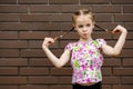 A child girl stands against a dark brick wall and playfully holds her pigtails Royalty Free Stock Photo