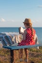 Child girl in a straw hat and dress sitting on bench and reading book. Cute kid with soft rabbit toy looking at notebook Royalty Free Stock Photo